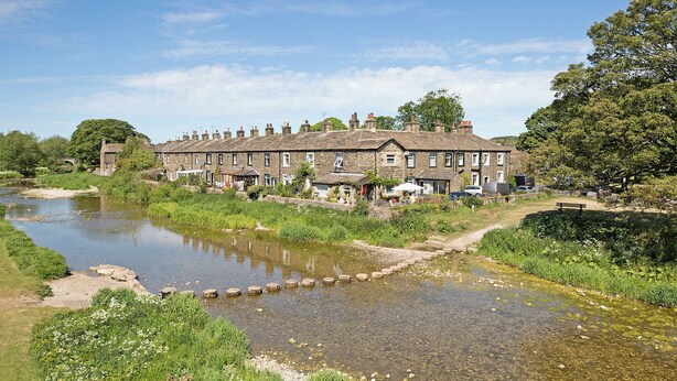 A riverside hotel with stone buildings, a clear river, and surrounding greenery. - An immaculately presented, 2 bedroom property with river views. (Gargrave)
