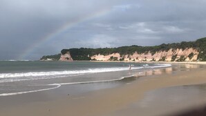 A beach with a rainbow, calm sea, and cliffs. - Macaco Surf Hostel (Tibau do Sul)