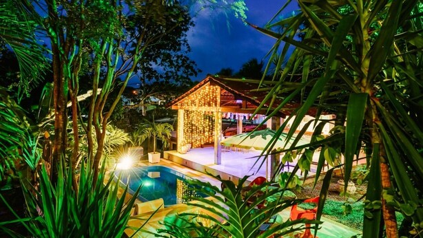A pool area with a covered seating area and a small structure decorated with lights. - Macaco Surf Hostel (Tibau do Sul)
