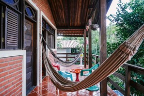 A covered outdoor area with a hammock, colorful chairs, and a table. - Macaco Surf Hostel (Tibau do Sul)