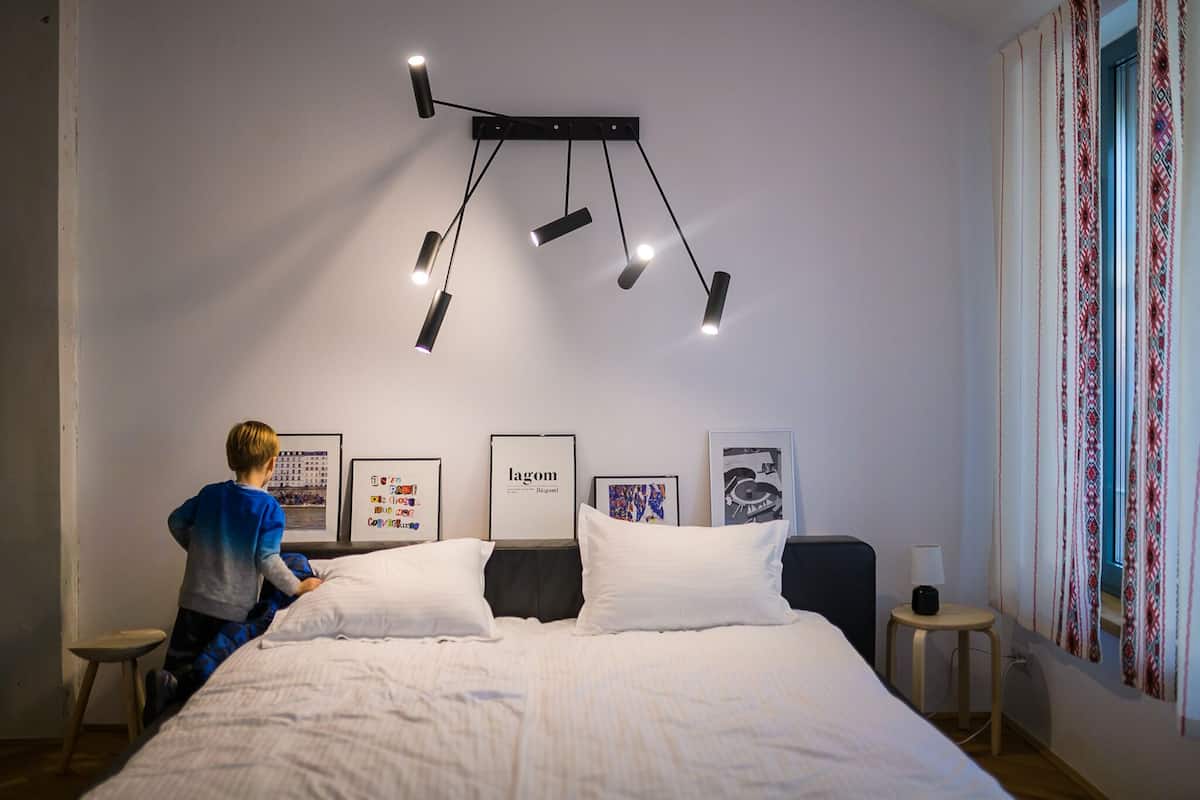 Une chambre à coucher avec un lit, un luminaire suspendu, des tableaux encadrés au mur et une fenêtre avec des rideaux.