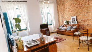 A living room with a brick wall, a brown leather sofa, a wooden desk, and a television.