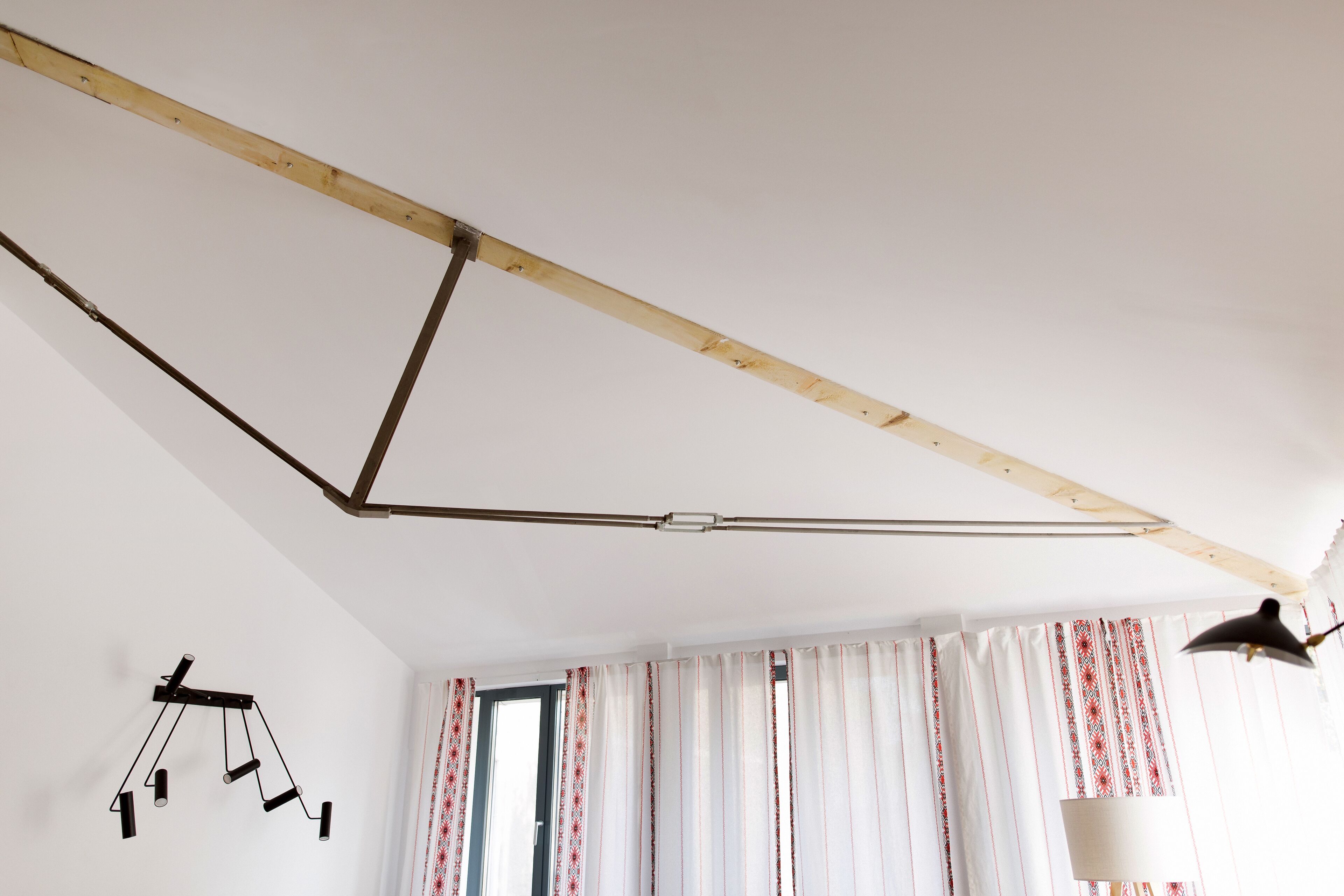 A room with a slanted ceiling, a hanging lamp, and a window with patterned curtains.