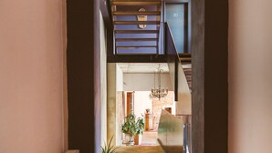 A narrow hallway with a wooden floor leading to a room with a large window, a chandelier, and a plant.