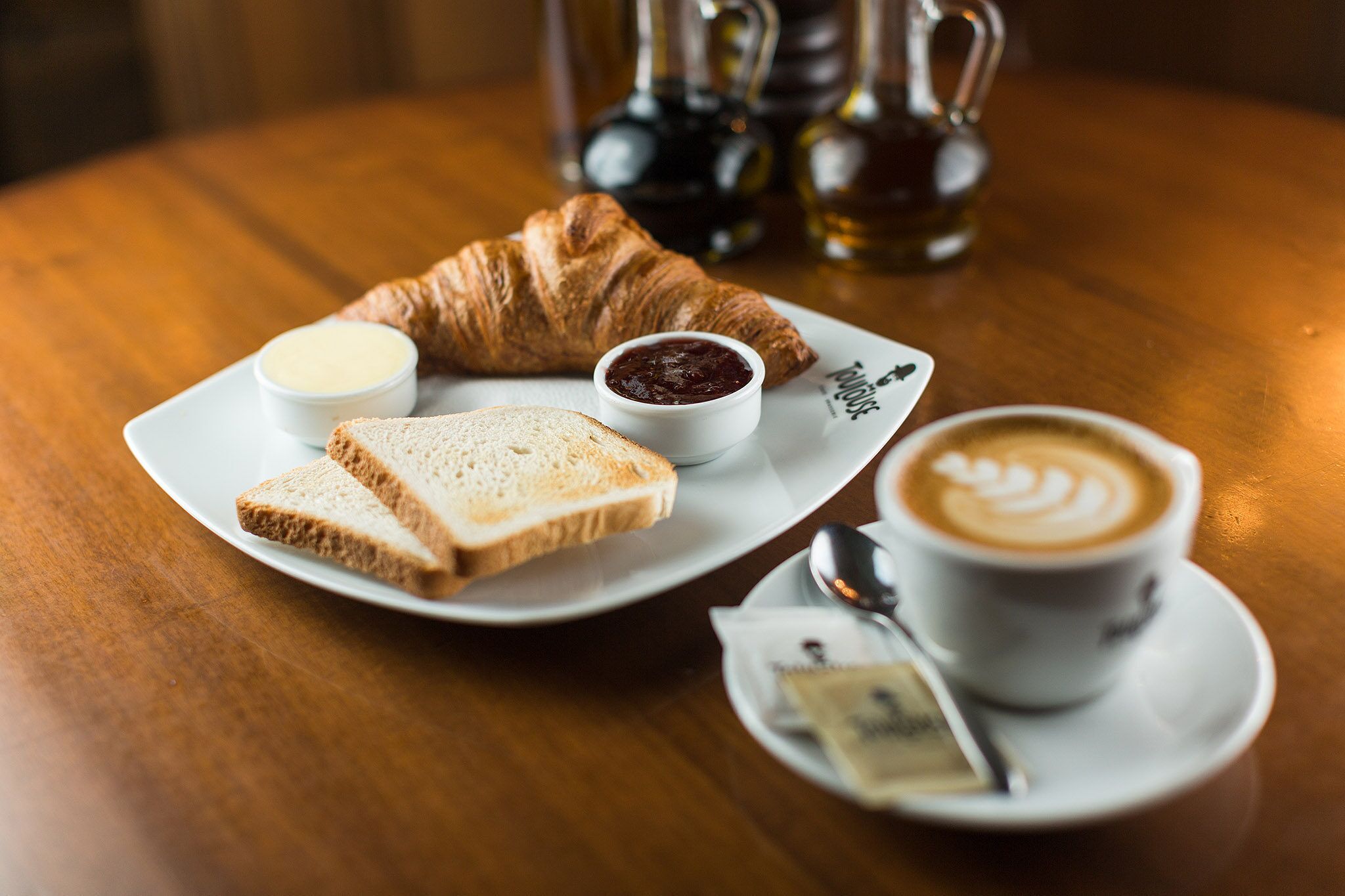 A croissant, two slices of bread, a small bowl of jam, and a cup of coffee on a white plate.