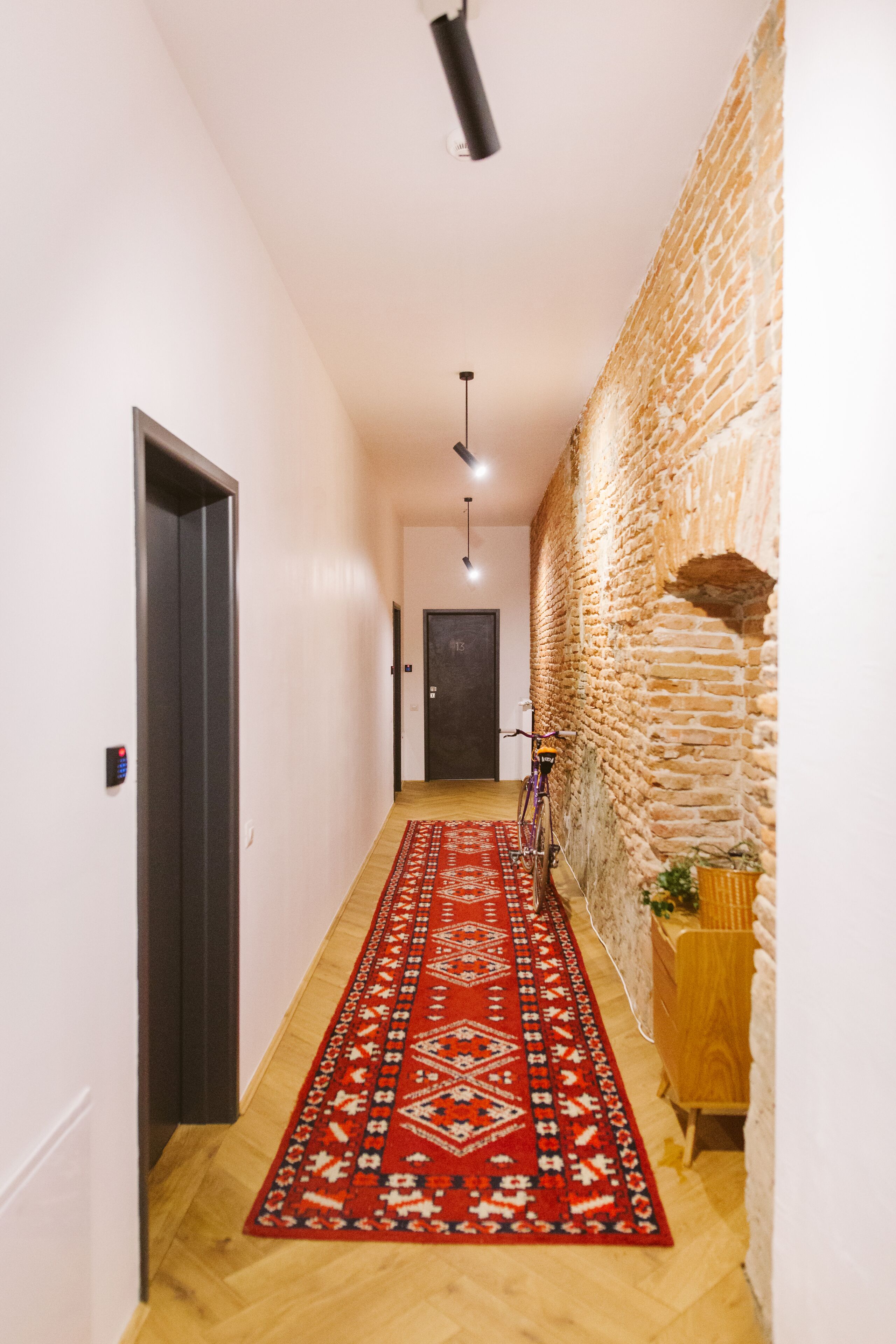 A hallway with a red patterned carpet, a wooden floor, a brick wall, and a door at the end.