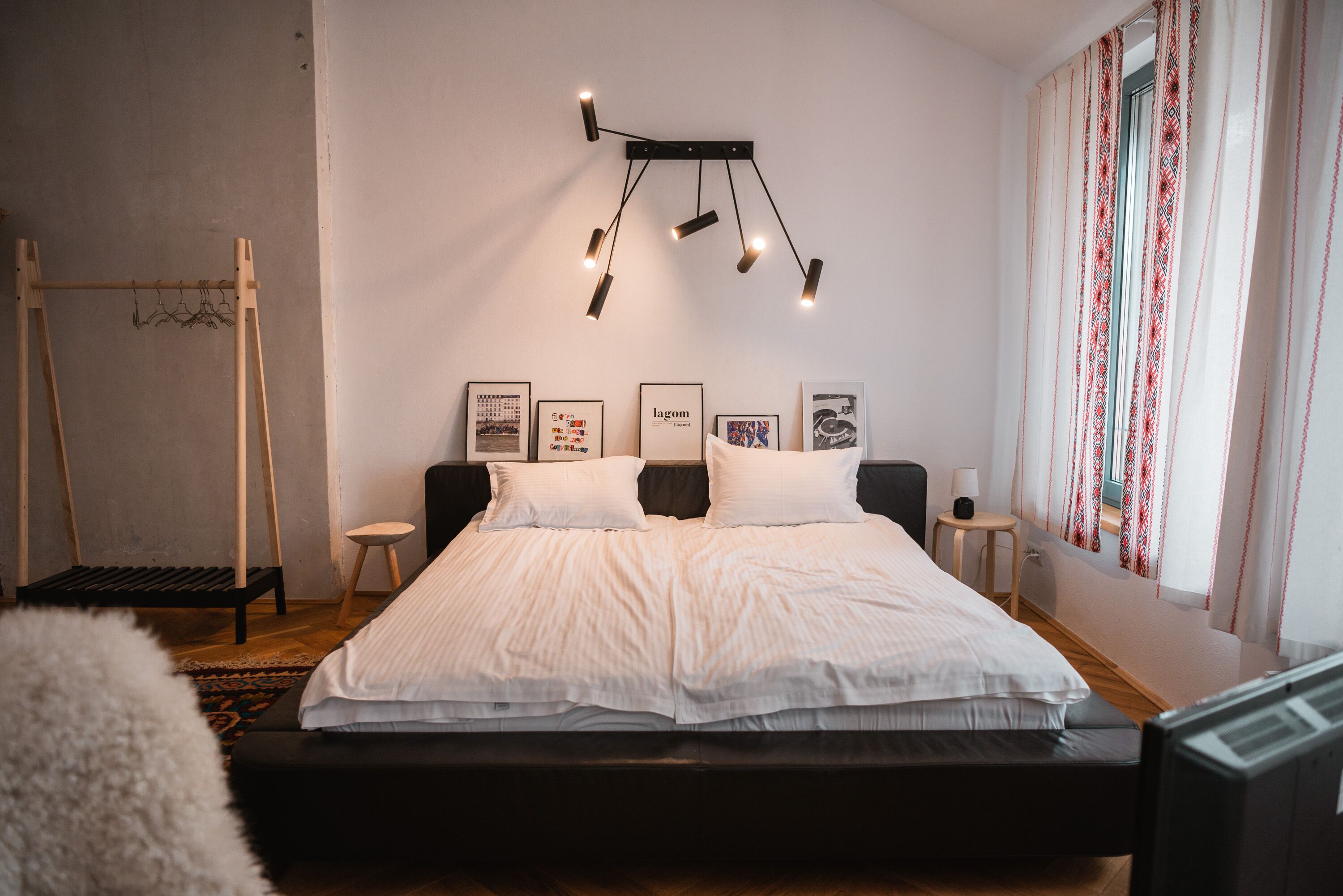 A bedroom with a bed, bedside tables, a hanging light fixture, and a window with curtains.