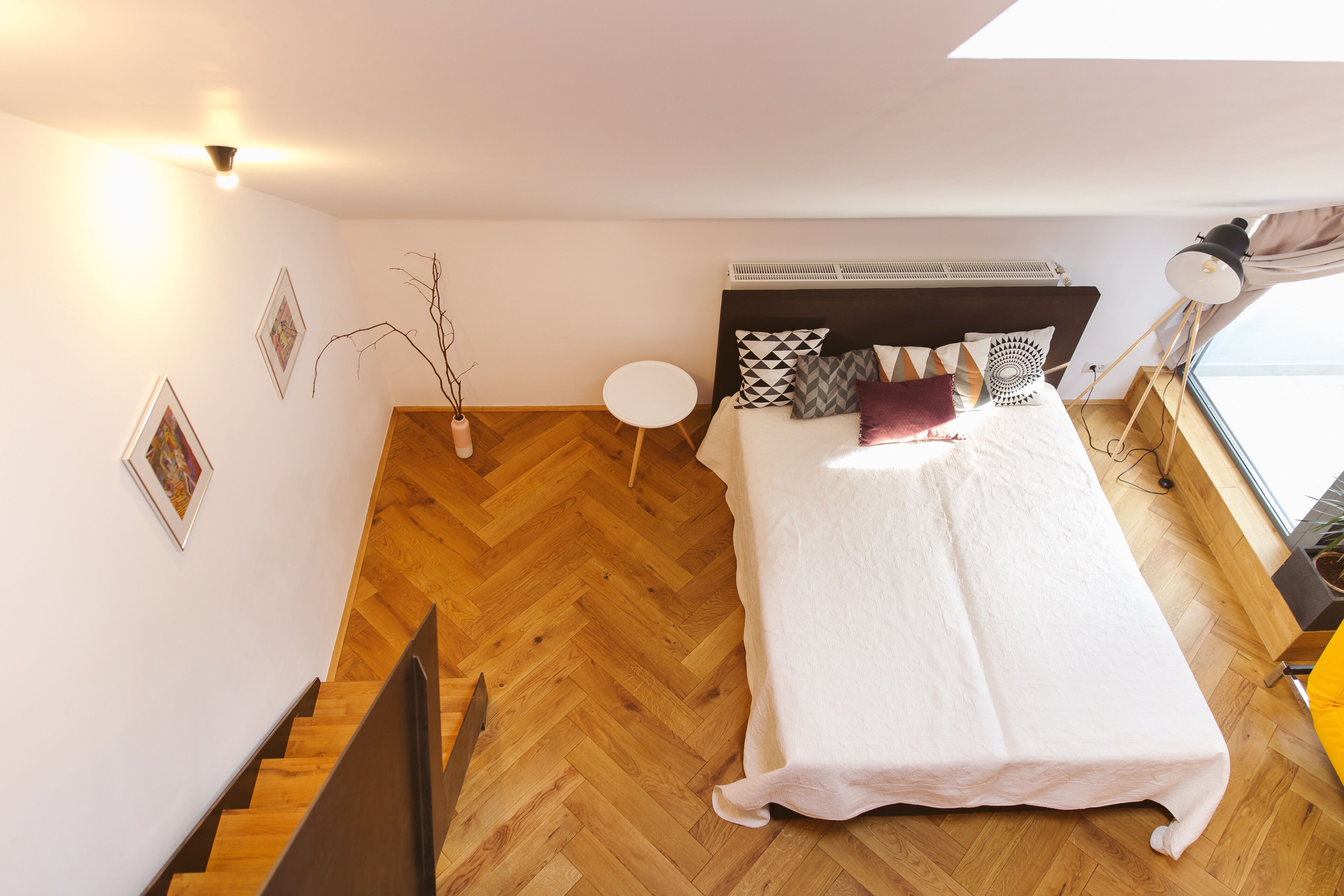 A bedroom with a bed, a small round table, a potted plant, and a window with curtains.
