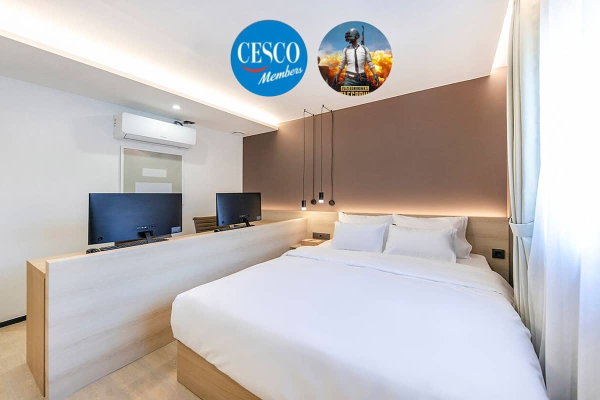 A hotel room with a bed, a desk with a flat-screen TV, and an air conditioning unit on the wall.
