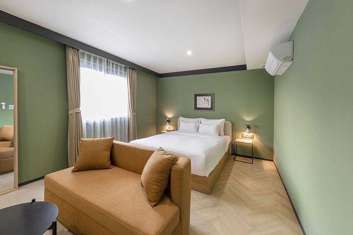 A hotel room with a bed, a sofa, a bedside table, and a mirror.