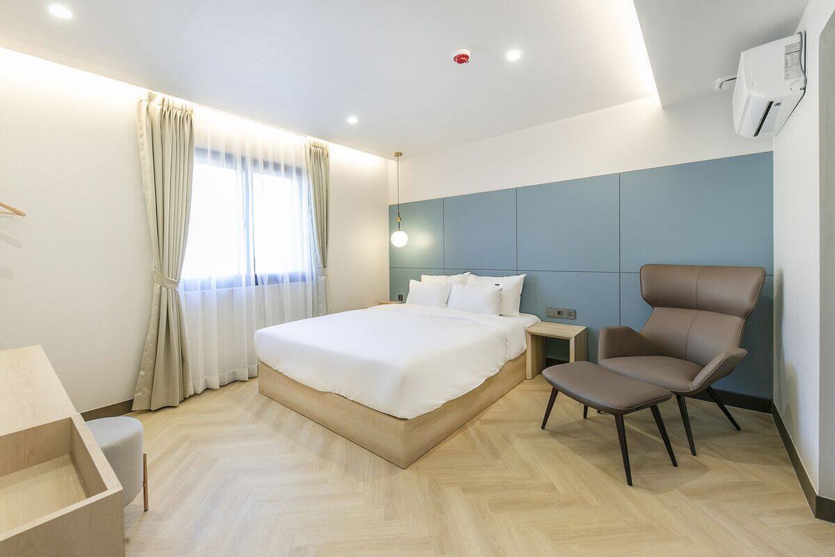 A modern hotel room with a large bed, a bedside table, a chair, and a window with curtains.