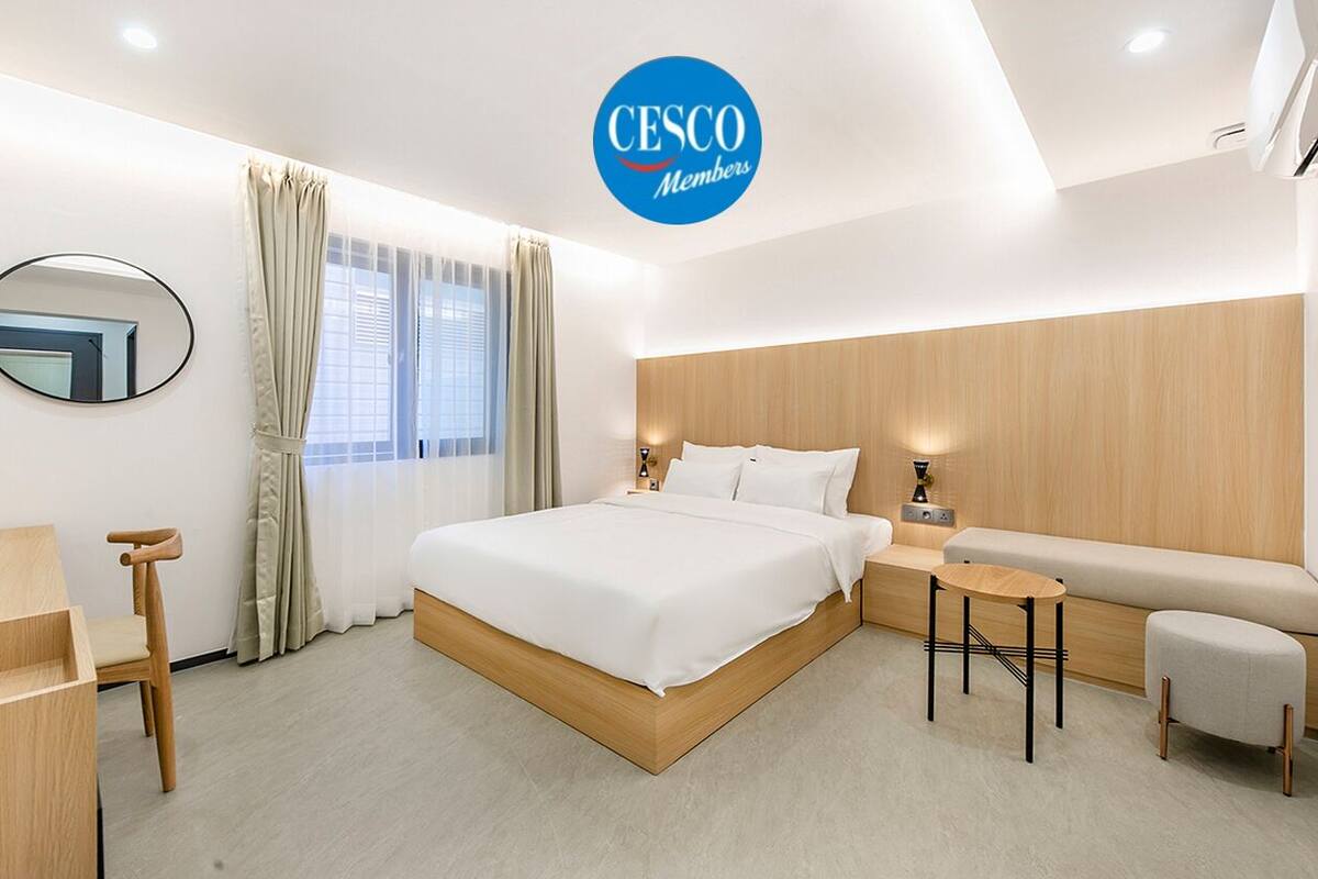 A modern hotel room with a large bed, a bedside table, a small round table, a sofa, and a chair.
