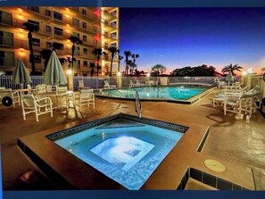 A hotel pool area with lounge chairs and umbrellas, surrounded by a fence and palm trees. - THE BEST SPOT ON THE BEACH!  5th floor NE corner unit! (Cocoa Beach)