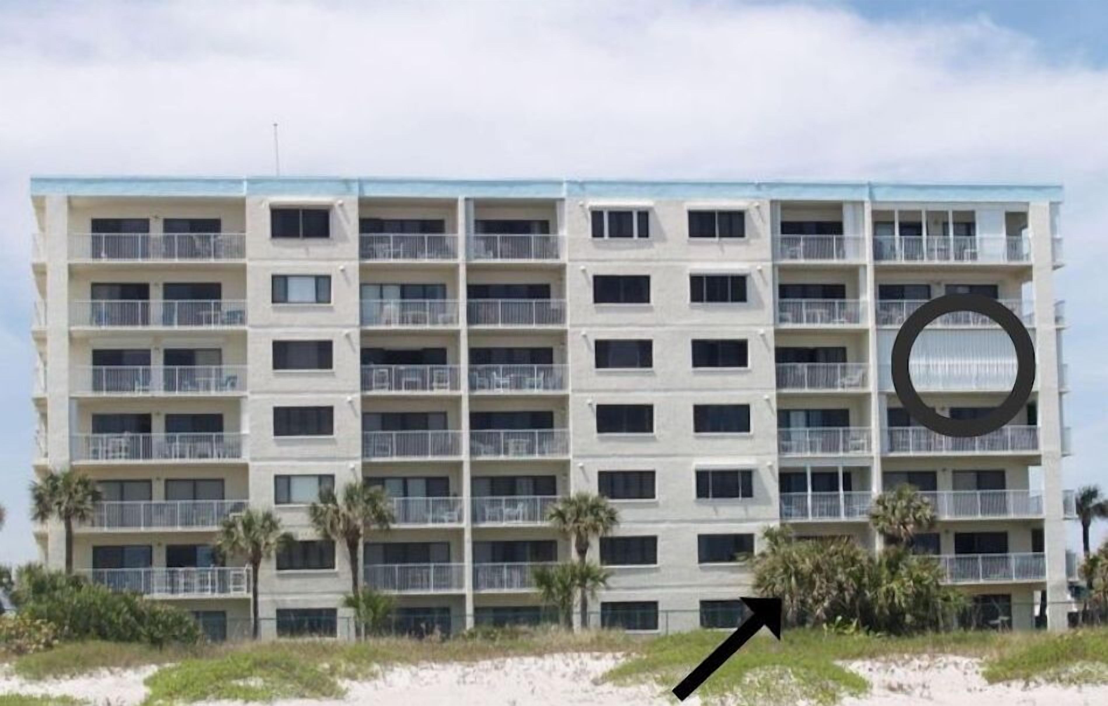A multi-story hotel with balconies, located near a beach.