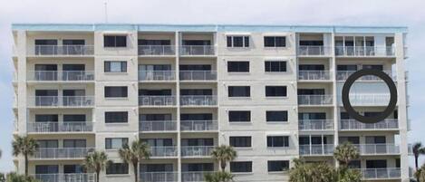 A multi-story hotel with balconies, located near a beach.