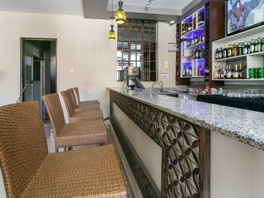 A bar area with wicker chairs, a bar counter, and shelves with bottles.
