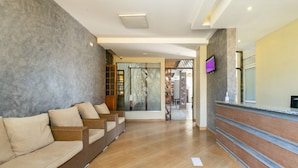 A reception area with a reception desk, a seating area with wicker sofas, and a view of the lobby. - Kings Premier Inn (Mlolongo)