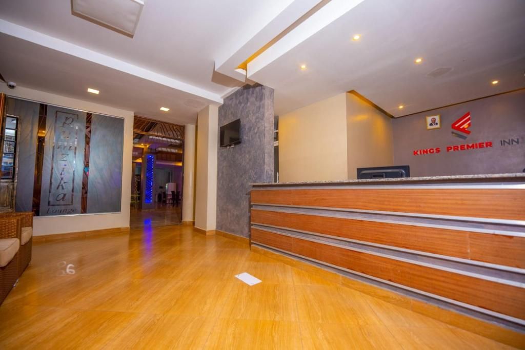 A hotel reception area with a wooden reception desk, a TV mounted on the wall, and a sign for 'Kings Premier Inn'.
