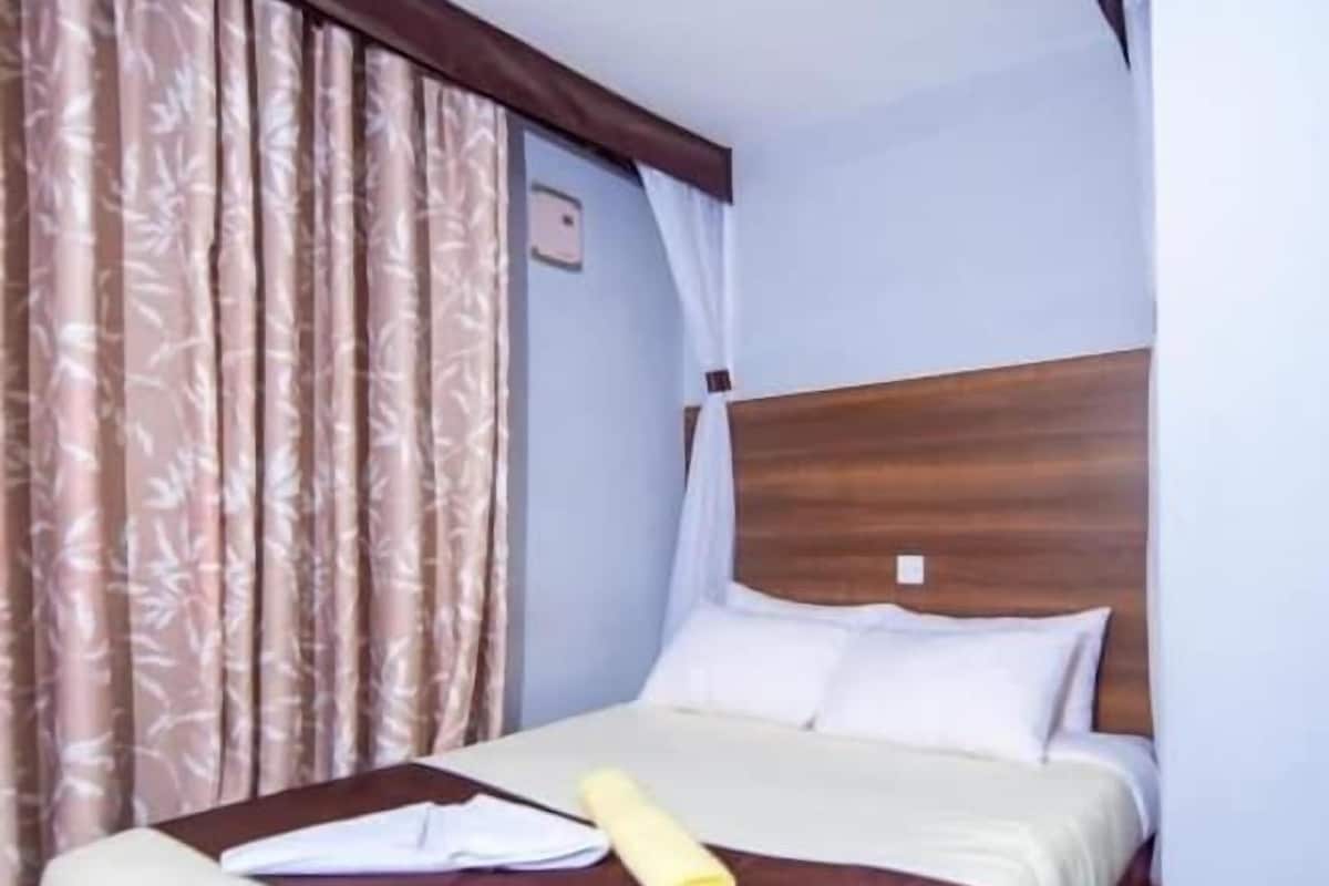 A hotel room with a bed, curtains, and a wooden headboard.