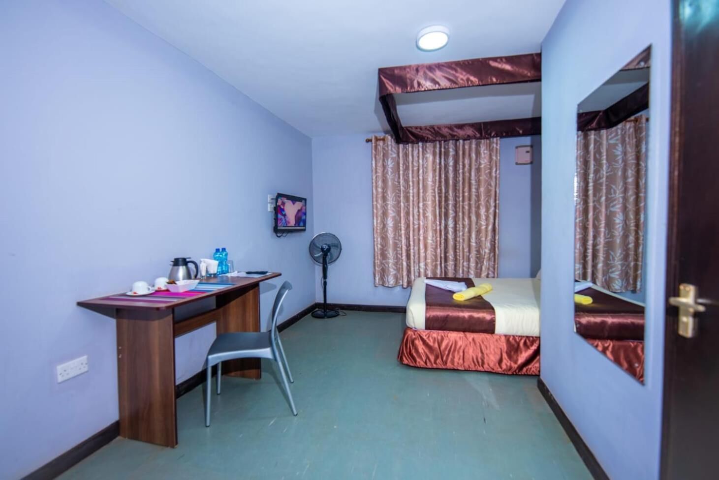 A compact room with a desk, chair, bed, and a fan.