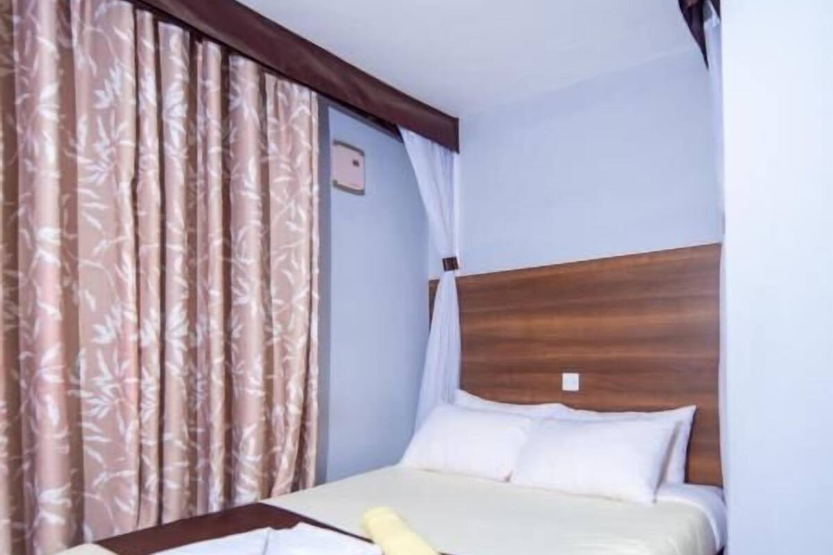 A hotel room with a bed, curtains, and a wooden headboard.