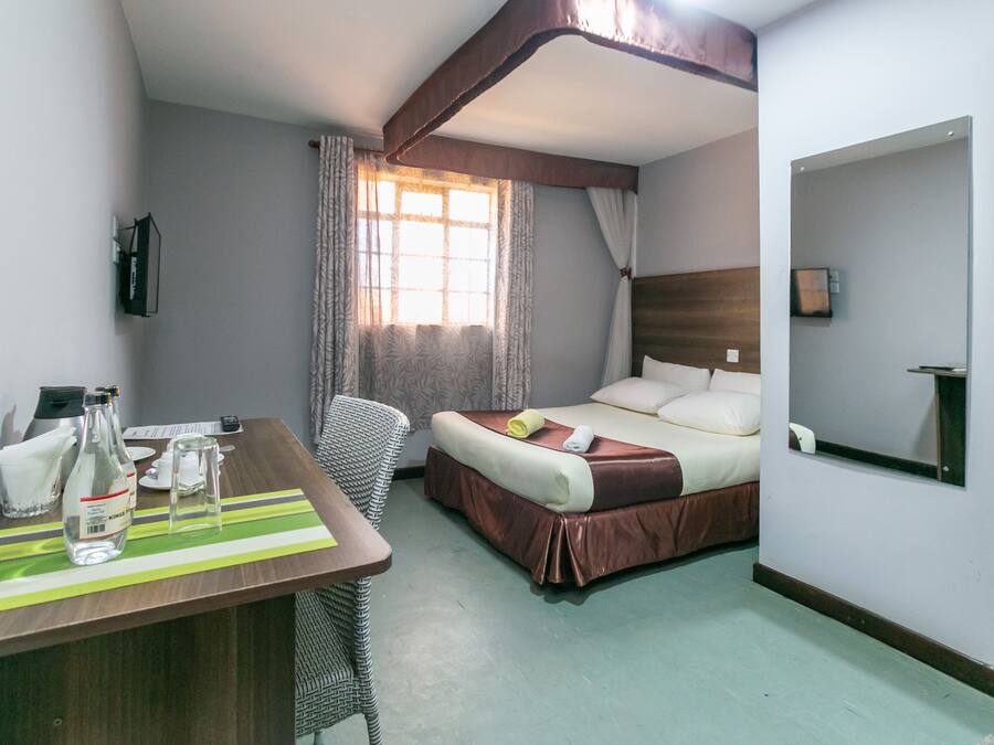 Habitación de hotel con cama, escritorio con silla, espejo y ventana con cortinas.