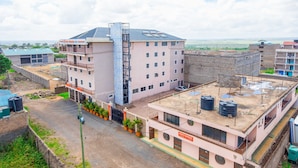 A multi-story hotel with a central staircase, a flat roof with water tanks, and a view of the surrounding area. - Kings Premier Inn (Mlolongo)