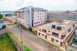 A multi-story hotel with a central staircase, a flat roof with water tanks, and a view of the surrounding area.