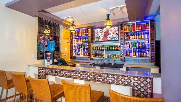 A bar area with wicker chairs, a counter, and shelves of liquor bottles. - Kings Premier Inn (Mlolongo)