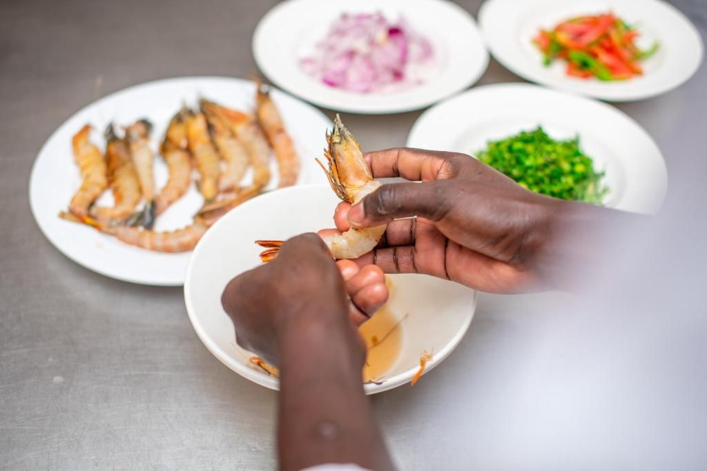 A person holding a shrimp, with plates of food in the background.