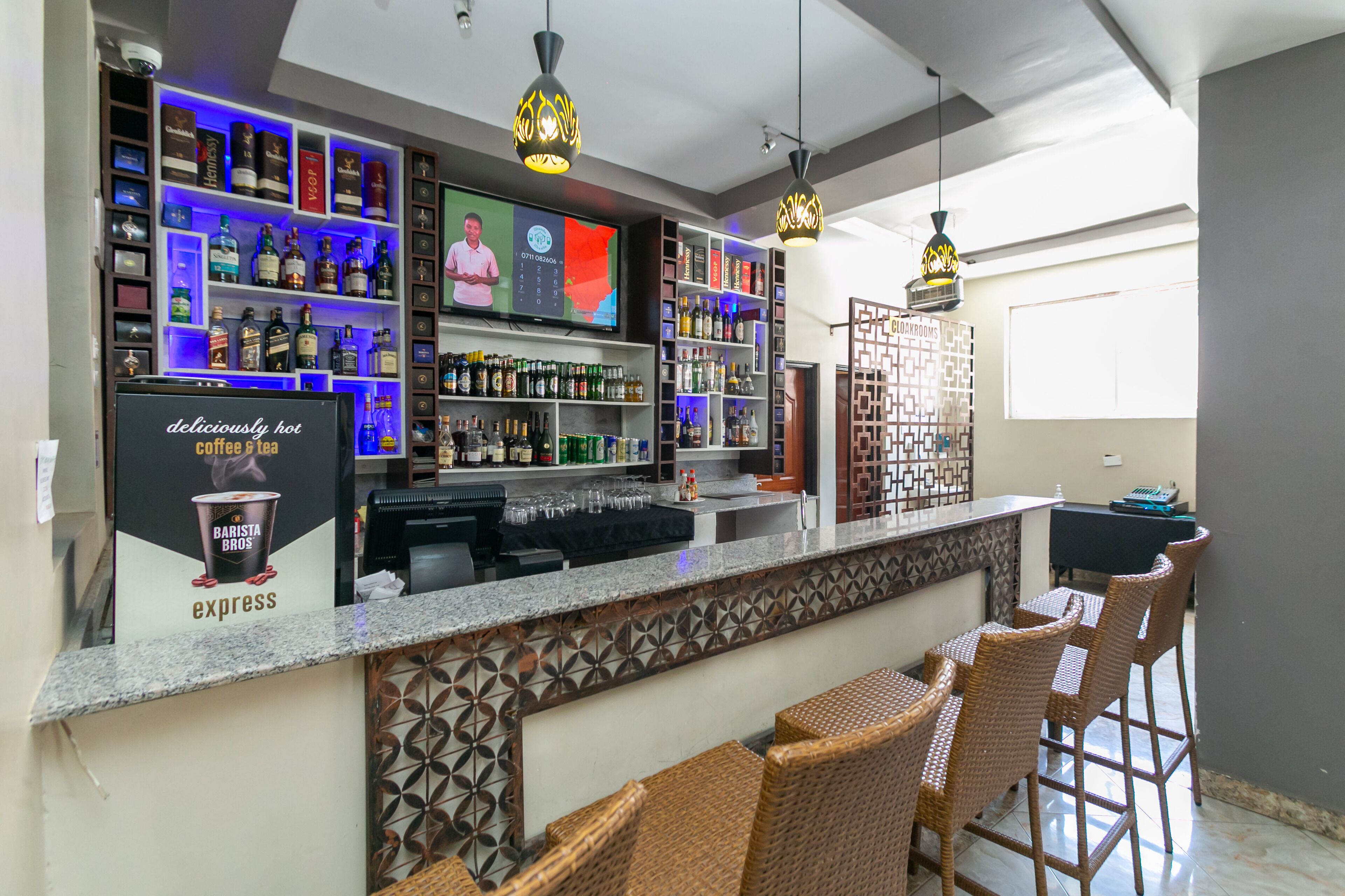 A bar area with shelves of liquor bottles, a coffee station, and wicker bar stools.