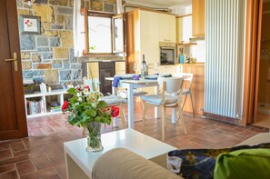 A cozy living room with a fireplace, a dining area with a table and chairs, and a kitchen in the background.