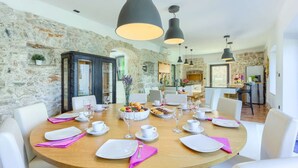 A dining area with a stone wall, a wooden table set for a meal, and black pendant lights. - Villa Cubismo - with a pool for 18 guests, close to restaurants and cafes by MyWaycation (Tkon)