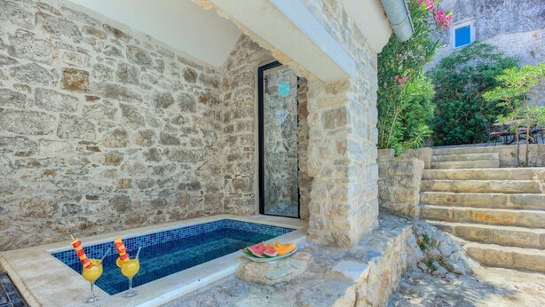 A stone-walled outdoor pool area with a glass door leading to a shower, surrounded by steps and greenery. - Villa Cubismo - with a pool for 18 guests, close to restaurants and cafes by MyWaycation (Tkon)