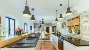 A modern kitchen with a stone wall, black pendant lights, and a wooden countertop. - Villa Cubismo - with a pool for 18 guests, close to restaurants and cafes by MyWaycation (Tkon)