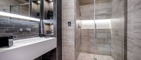 A modern bathroom with a glass-enclosed shower, a white sink with a black soap dispenser, and a mirror with built-in lighting.