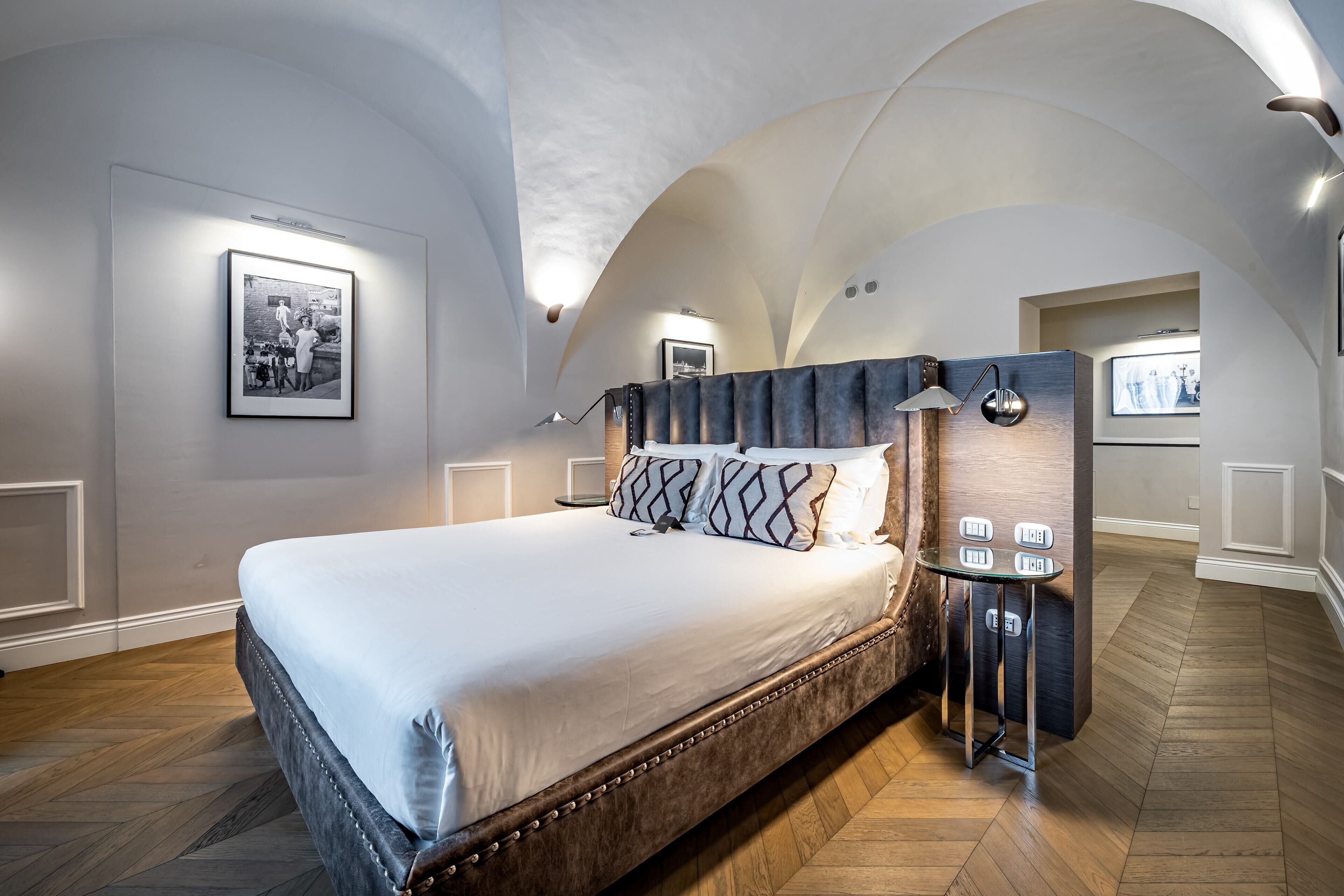 Une chambre d’hôtel moderne avec un grand lit, une tête de lit en bois et une petite table avec une lampe.