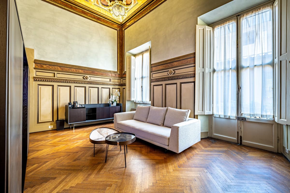A spacious living room with a wooden parquet floor, a beige sofa, a glass coffee table, and a dark-colored entertainment unit.