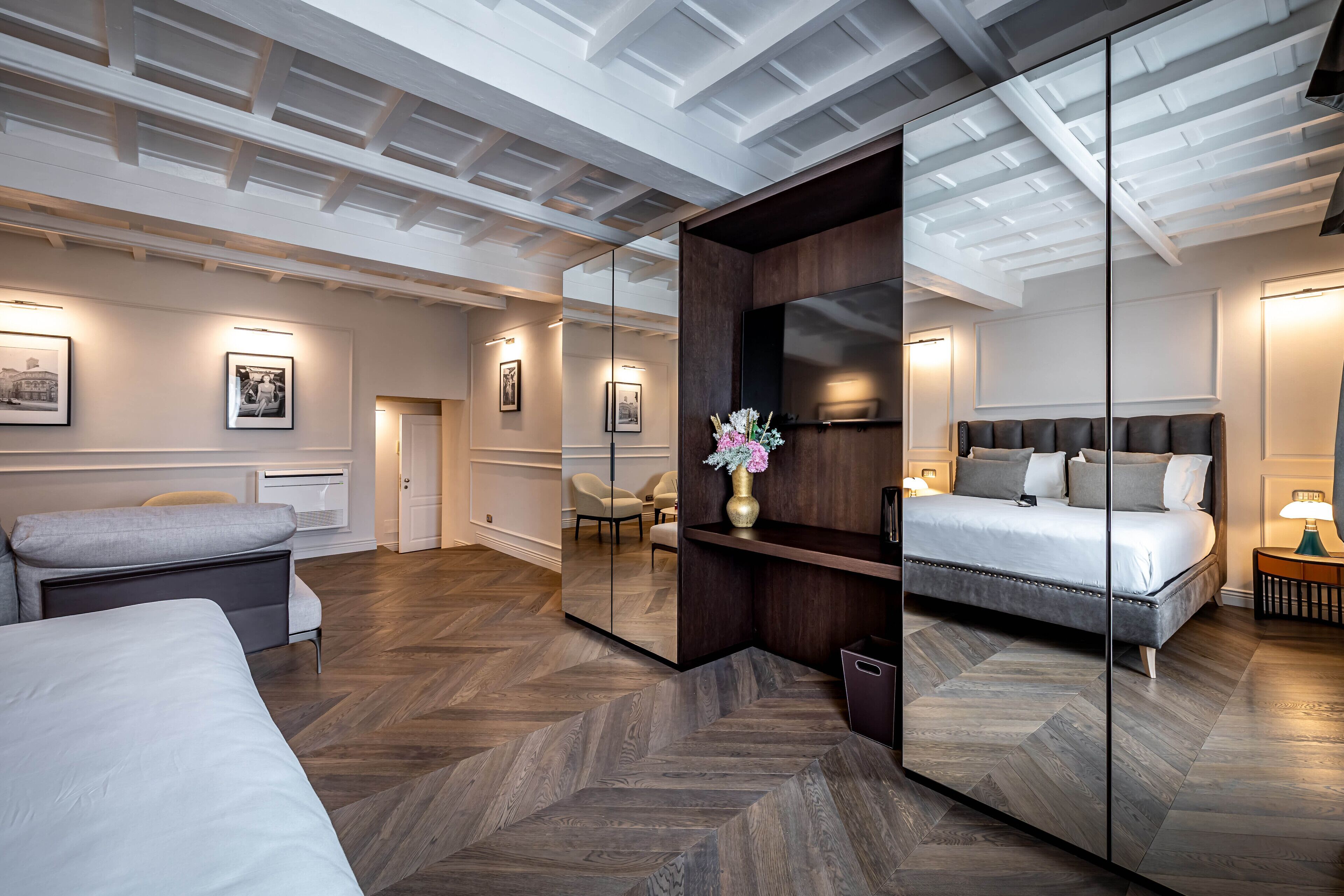 A modern hotel room with a large bed, a sofa, a mirror, and a wooden floor.