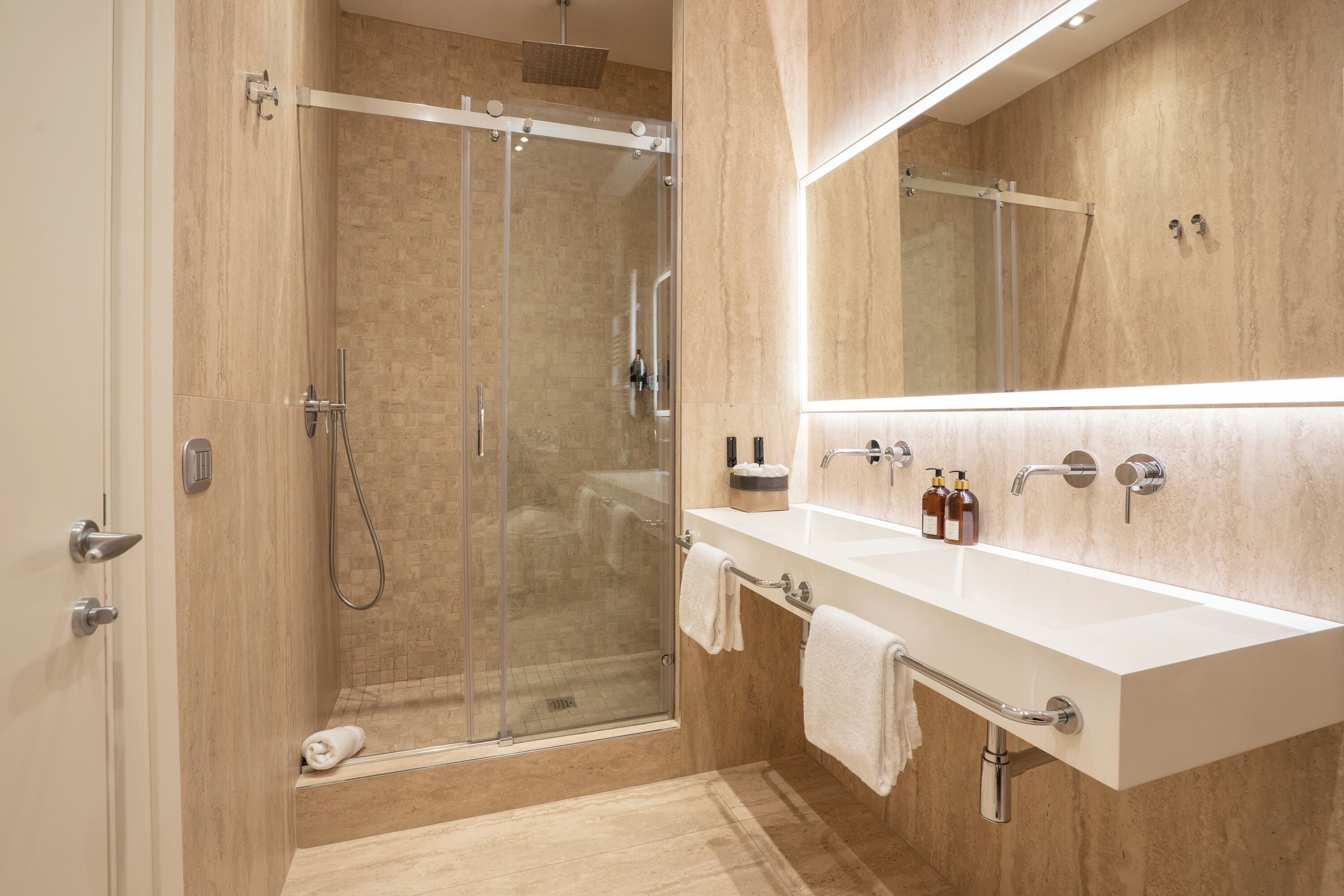 A modern bathroom with a glass-enclosed shower, a white vanity with a mirror, and a beige tiled floor.
