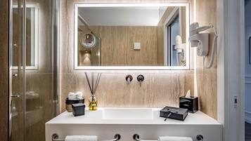 A modern bathroom with a large mirror, two sinks, a hairdryer, and a towel rack.