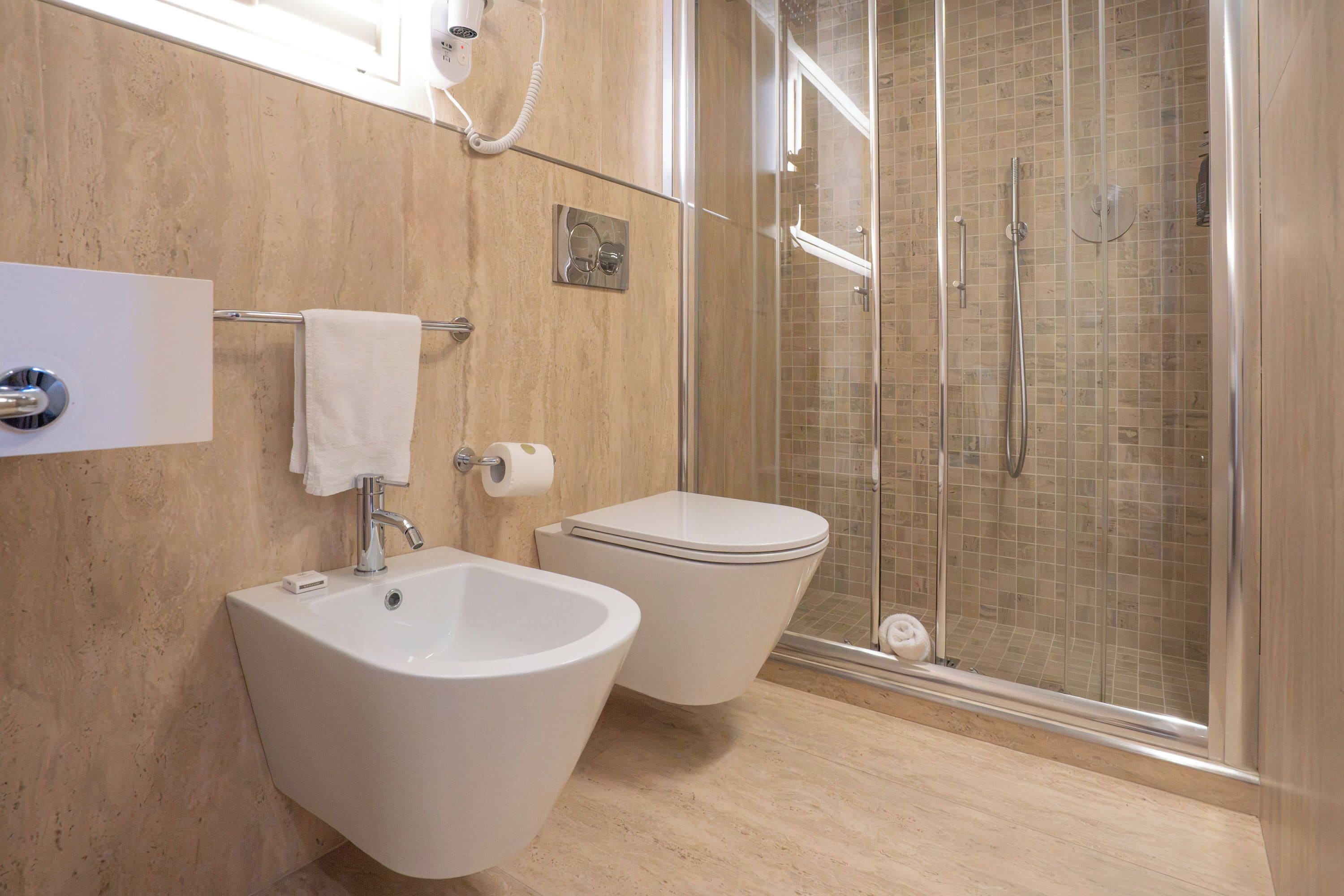 Un baño con bidé, inodoro y ducha con mampara de vidrio.