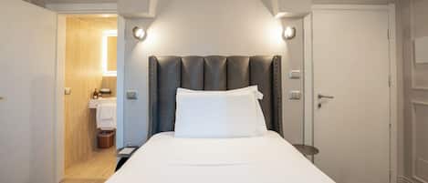 Habitación de hotel con cama, mesita de noche, un baño visible a través de una puerta abierta.