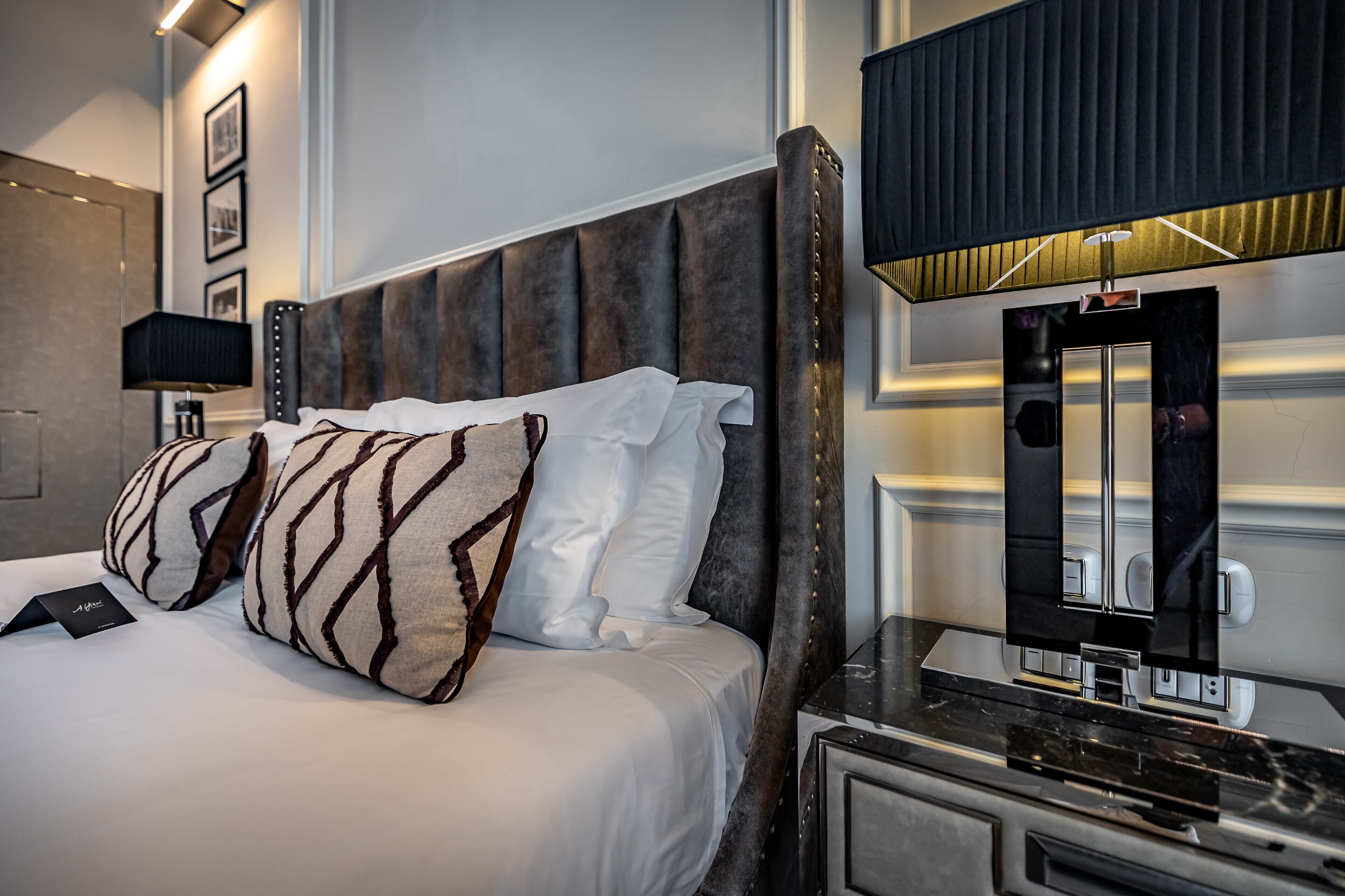 Una habitación de hotel con una cama, almohadas, una mesita de noche, una lámpara y un espejo.