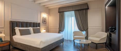 A hotel room with a large bed, two armchairs, a small round table, and a TV.