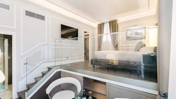 A hotel room with a glass-enclosed balcony, a bed, a TV, and a dining area with a table and chairs.