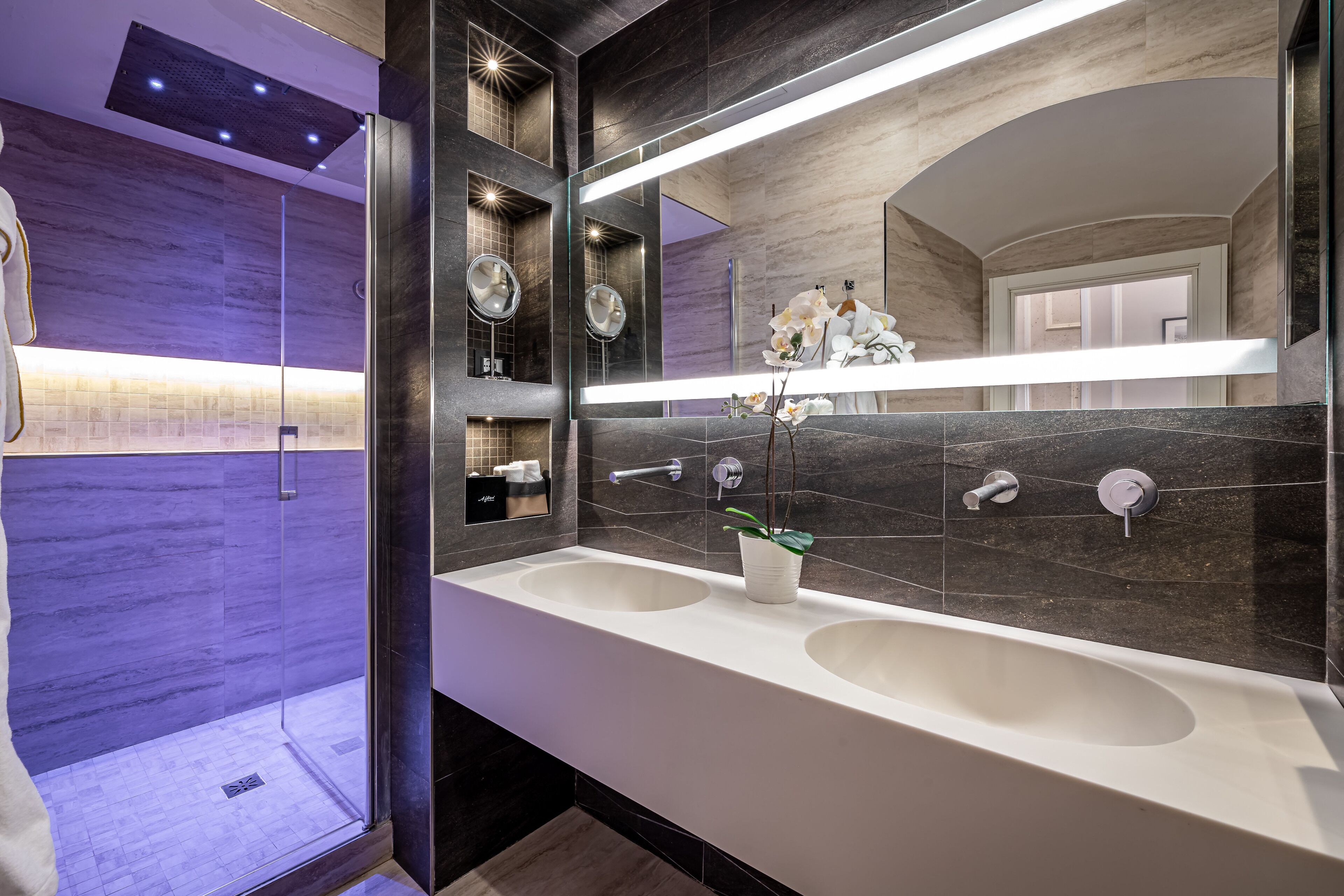 A modern bathroom with two sinks, a large mirror, and a glass shower enclosure.