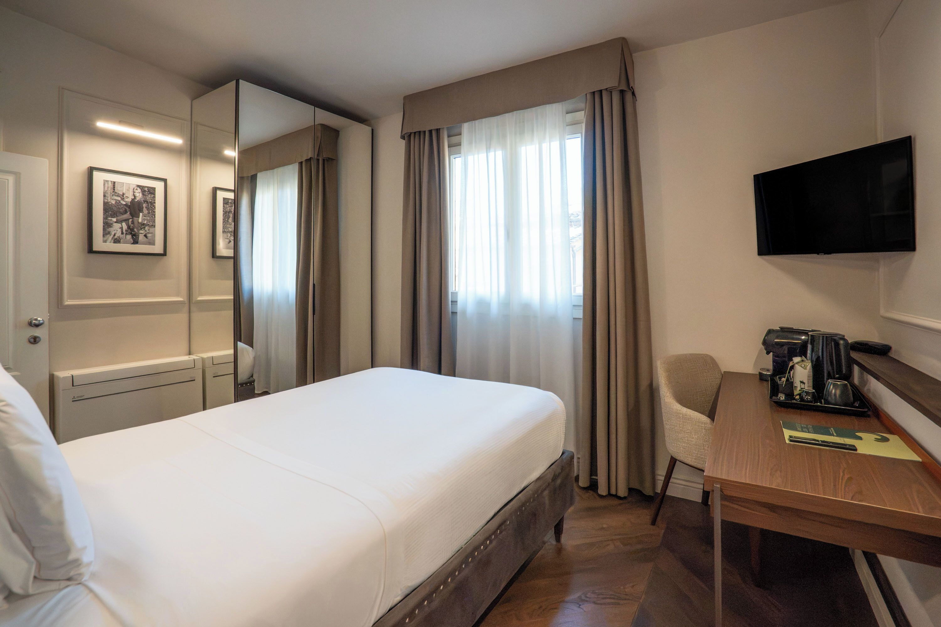 Une chambre d’hôtel équipée d’un lit, d’un bureau, d’une chaise, d’une télévision, d’un miroir et de rideaux.