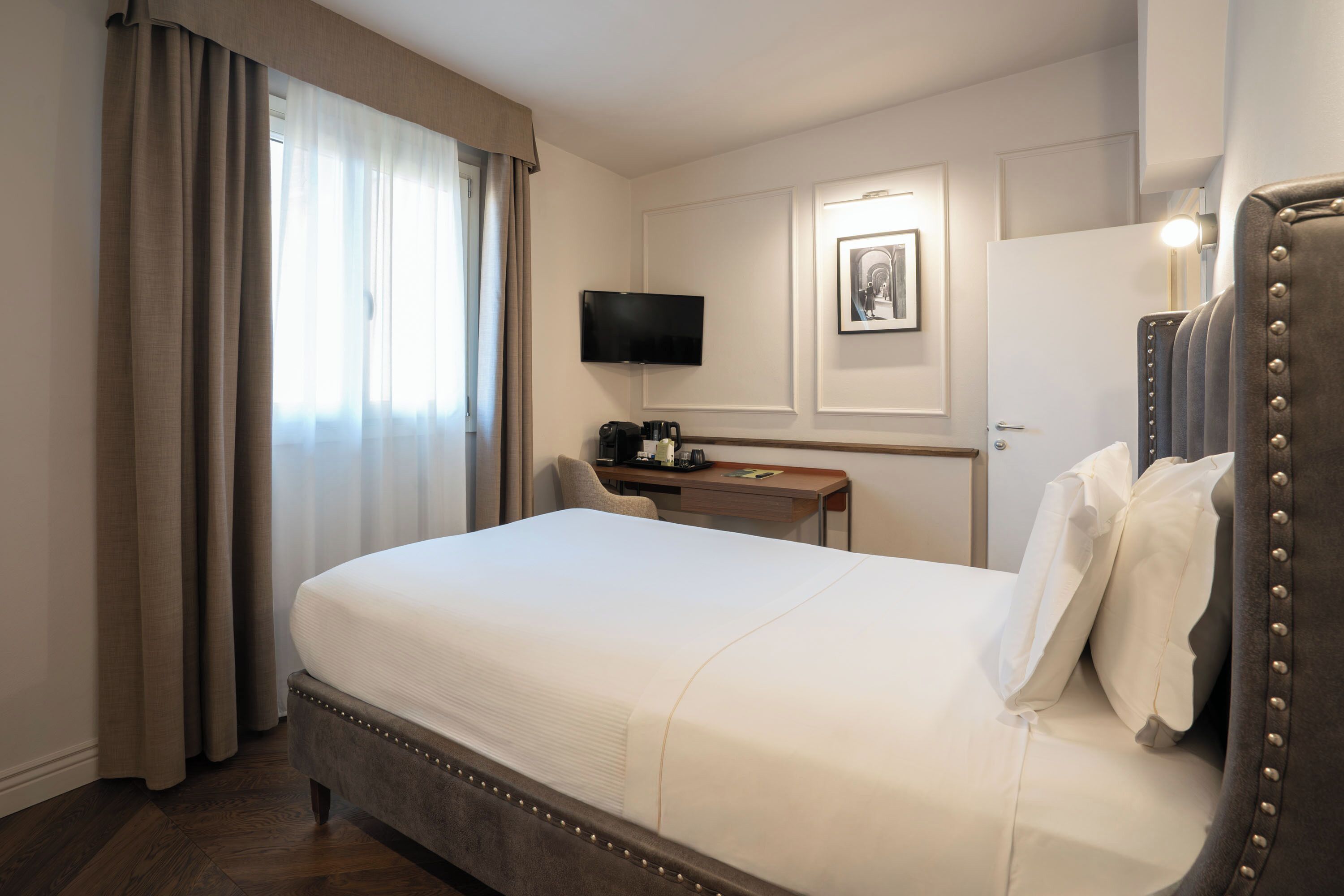 A hotel room with a large bed, a desk, a television, and a framed picture on the wall.