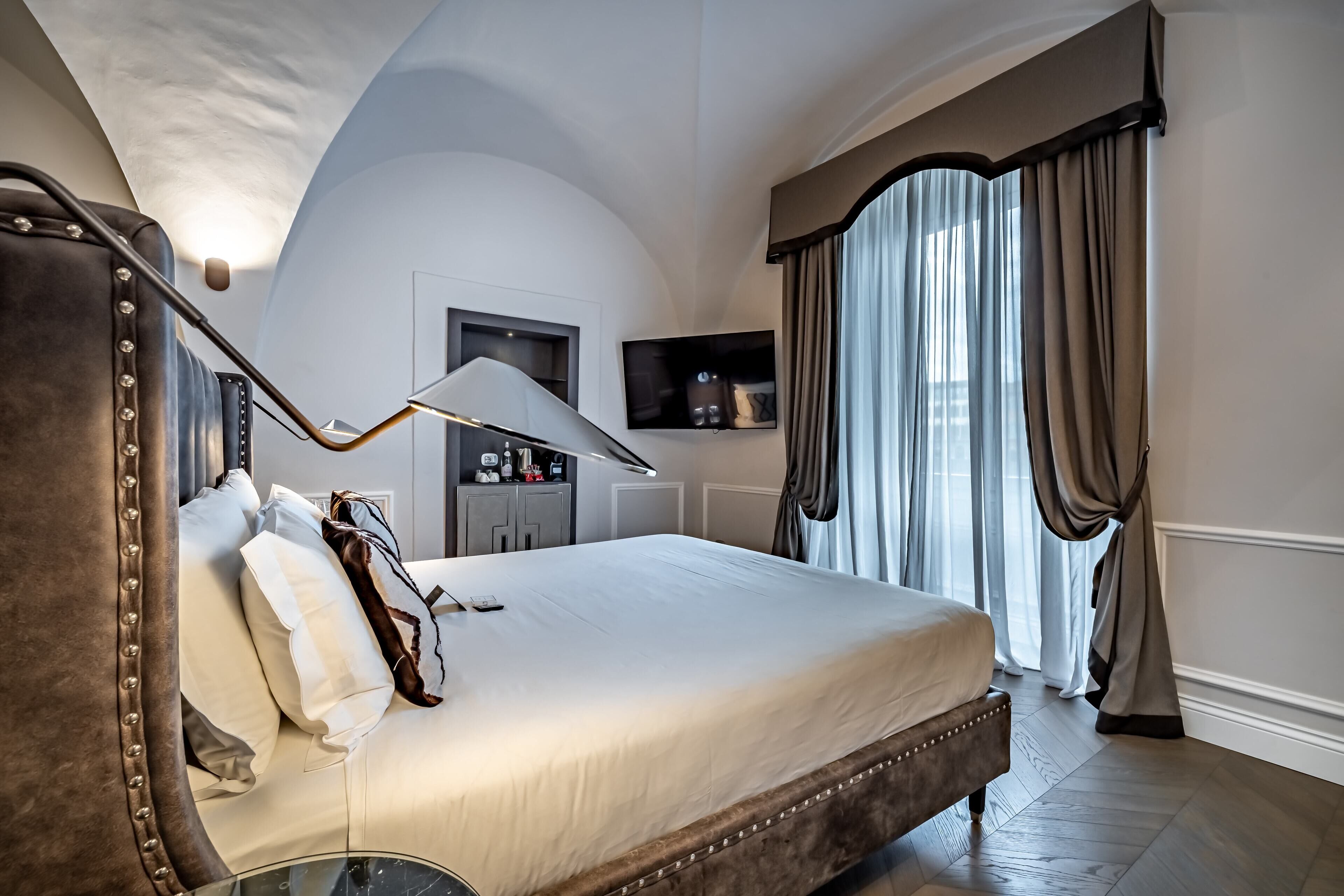A bedroom with a large bed, a bedside table, a lamp, a wardrobe, and a TV on the wall.